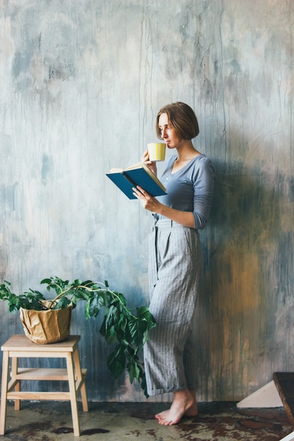 Jonge vrouw met gele kop die zich tegen muur bevinden en boek in de studio van het kunstwerk lezen