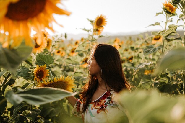 Jonge vrouw met gesloten ogen die midden in zonnebloemen staat.