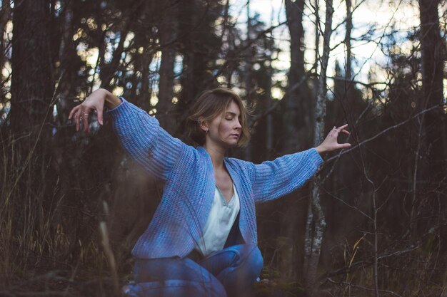 Foto jonge vrouw met gesloten ogen die tegen bomen in het bos danst.