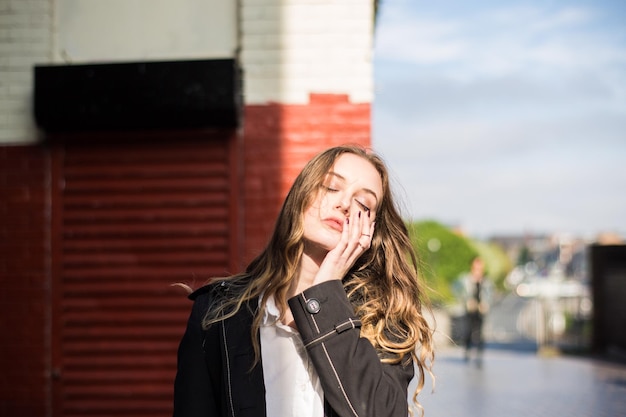 Jonge vrouw met gesloten ogen die tegen de muur staat.