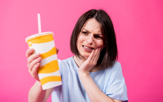 Jonge vrouw met gevoelige tanden die koud water drinken op gekleurde achtergrond