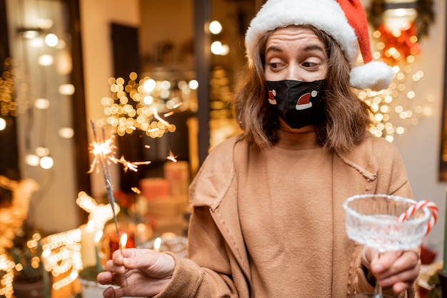 Jonge vrouw met gezichtsmasker die alleen nieuwjaarsvakantie thuis viert. Concept van quarantaine en zelfisolatie tijdens de epidemie op feestdagen