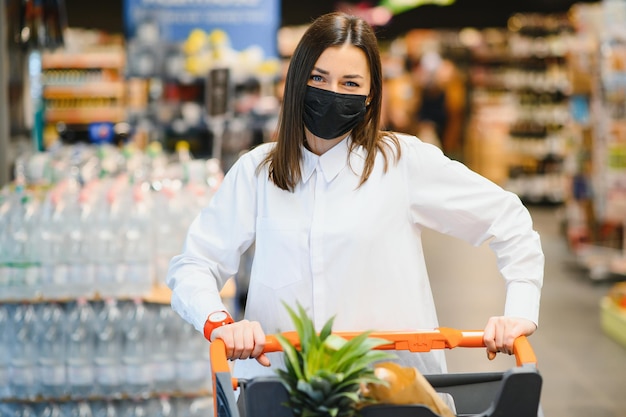 Jonge vrouw met gezichtsmasker die door de supermarkt loopt tijdens de COVID-19-pandemie.