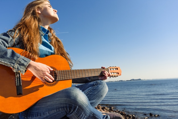 Jonge vrouw met gitaar buiten op zeekust