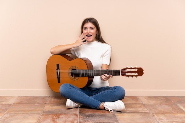 Jonge vrouw met gitaarzitting op de vloer met verrassingsgelaatsuitdrukking
