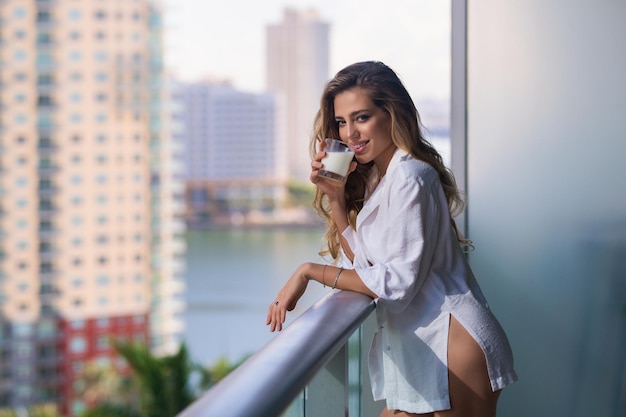 Jonge vrouw met glas melk op balkon terras meisje consumptiemelk thuis mooie vrouw bedrijf