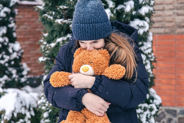 Jonge vrouw met haar favoriete teddybeer in haar armen in de winter