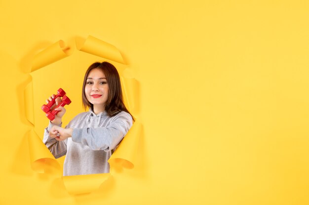 jonge vrouw met halters op gele achtergrond gym fit oefeningen atleet