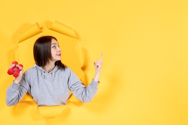 jonge vrouw met halters wijzend naar iets op geel papier achtergrond oefening atleten