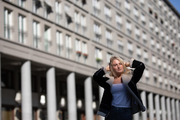 Jonge vrouw met hand in haar die tegen het gebouw staat