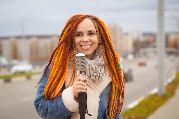 Jonge vrouw met heldere dreadlocks met retro microfoon op straat in de stad Portret van zangeres die in de microfoon zingt bij bewolkt weer
