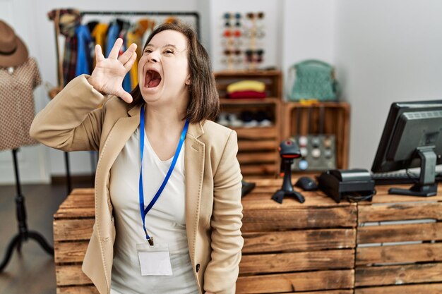 Jonge vrouw met het syndroom van Down werkt als manager in een boetiek in de detailhandel en schreeuwt en schreeuwt luid naar de zijkant met de hand op de mond. communicatieconcept.