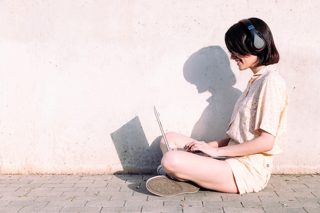 Jonge vrouw met hoofdtelefoons die met laptop werken
