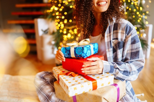 Jonge vrouw met kerstcadeaus thuis in de buurt van de kerstboom Wintervakanties Oud en Nieuw