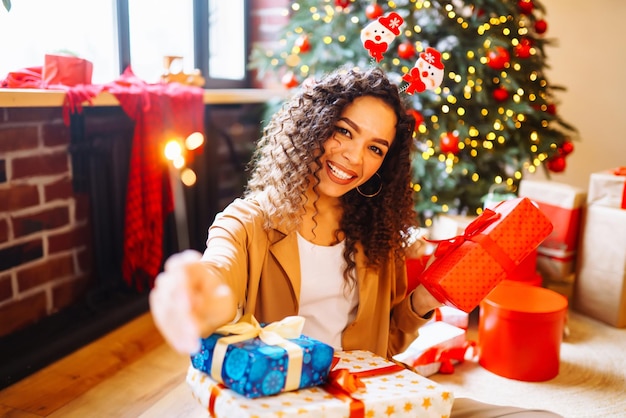 Jonge vrouw met kerstcadeaus thuis in de buurt van de kerstboom Wintervakanties Oud en Nieuw