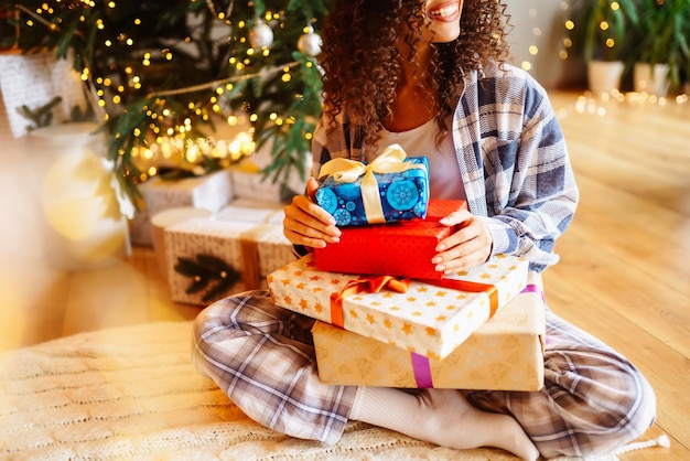 Jonge vrouw met kerstcadeaus thuis in de buurt van de kerstboom Wintervakanties Oud en Nieuw