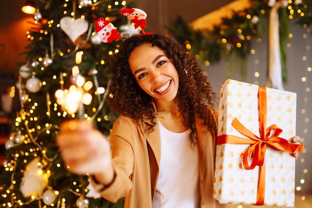 Jonge vrouw met kerstcadeaus thuis in de buurt van de kerstboom Wintervakanties Oud en Nieuw