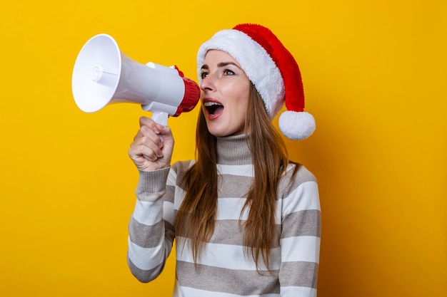 Jonge vrouw met kerstmuts spreekt in een megafoon op een gele achtergrond