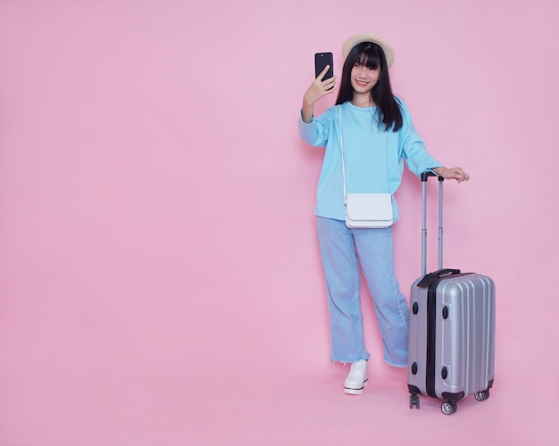 Jonge vrouw met koffer en smartphone op roze muur