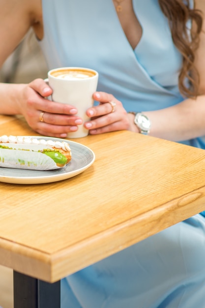 Jonge vrouw met kopje koffie en fluitje van een cent zittend aan de tafel in een café buitenshuis