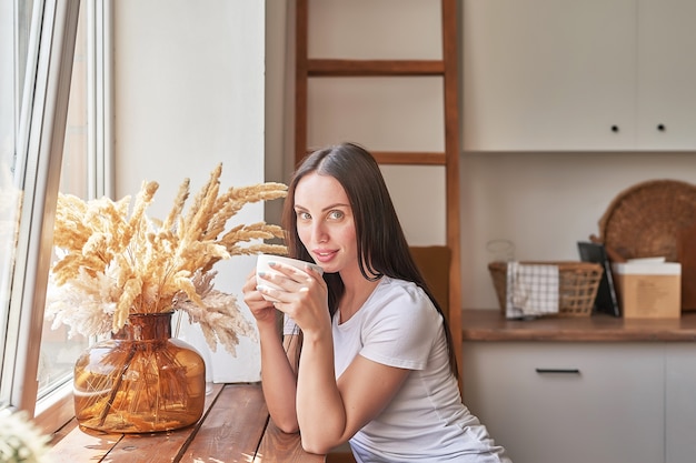 Jonge vrouw met kopje koffie of thee bij raam in coffeeshop. Goedemorgen concept. Gezellig ontbijt. Meisje in café.