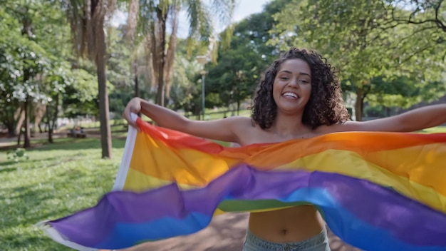 Jonge vrouw met krullend haar die bedekt is met de vlag van de lgbt-trots. Vuist omhoog houden, LGBT+ vlag bedekken