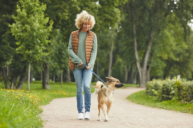 Jonge vrouw met krullend haar die samen met haar huisdier langs het pad in het park loopt