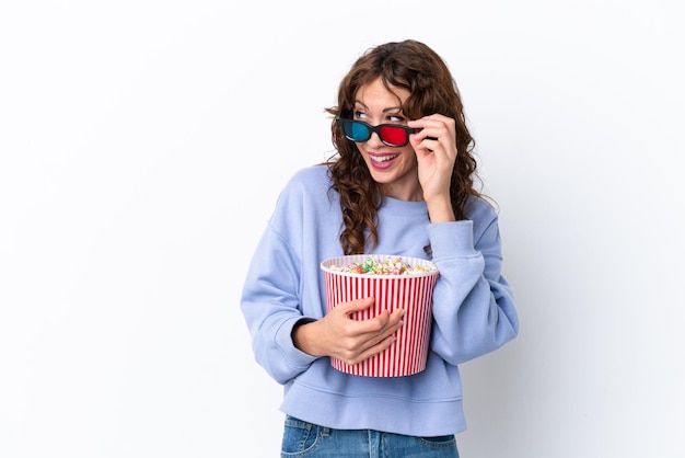 Foto jonge vrouw met krullend haar geïsoleerd op een witte achtergrond met 3d-bril en met een grote emmer popcorns