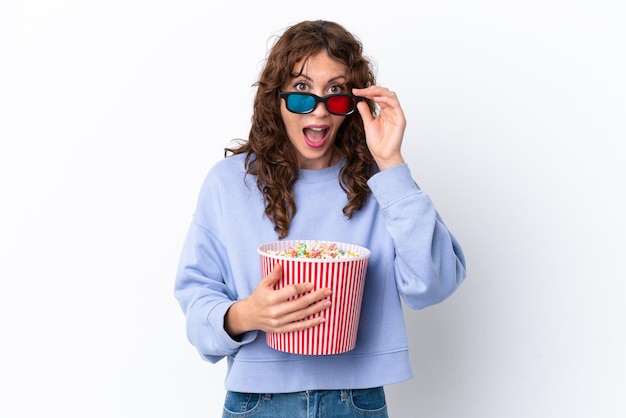 Jonge vrouw met krullend haar geïsoleerd op een witte achtergrond verrast met 3D-bril en met een grote emmer popcorns