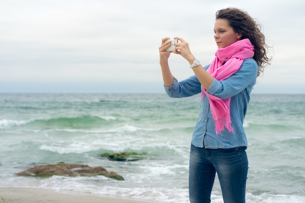 Jonge vrouw met krullend haar maakt de foto van de kust