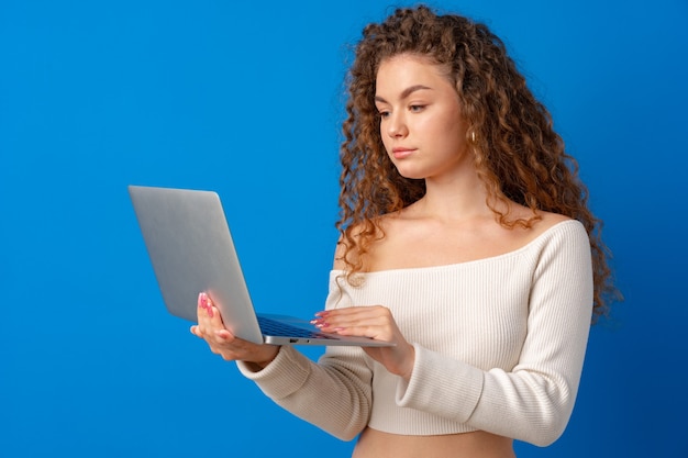 Jonge vrouw met krullend haar met laptop tegen blauwe achtergrond