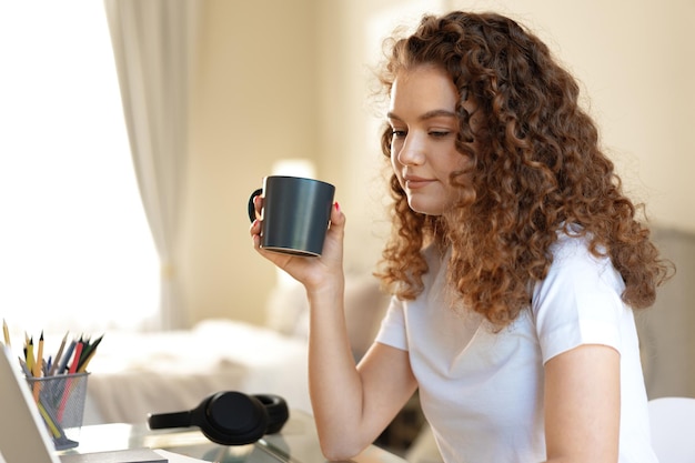 Jonge vrouw met krullend haar ontspannen binnenshuis thuis met een kopje koffie