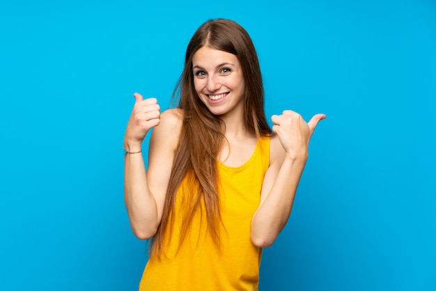 Jonge vrouw met lang haar over geïsoleerde blauwe muur met thumbs up gebaar en glimlachen