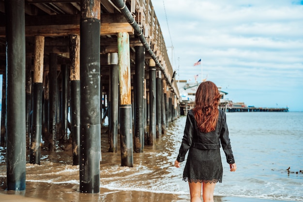 jonge vrouw met lang haar staat in de buurt van de pier op het strand in santa barbara californië usa