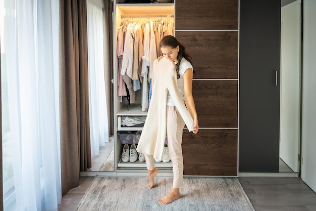 Foto jonge vrouw met lang krullend donker haar staat in de kast en kiest oude ongewenste kleren te koop