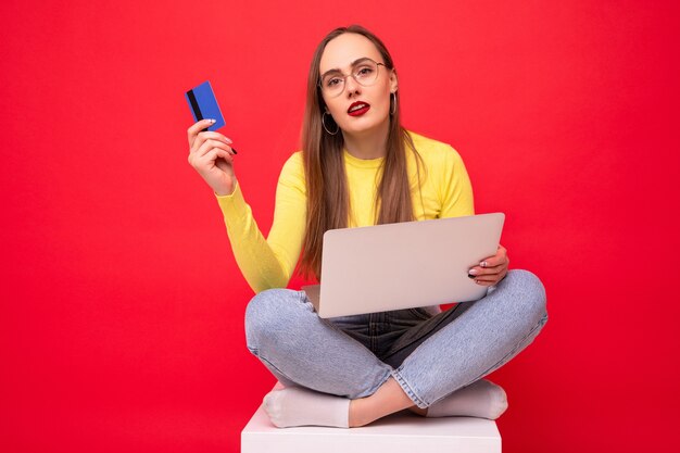 Jonge vrouw met laptop en bankkaart op rode achtergrond