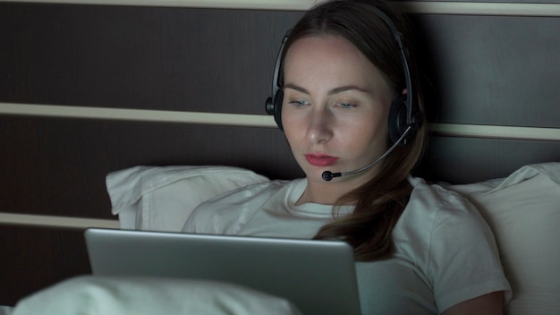 Jonge vrouw met laptop headset werken vanuit huis video-oproep in de slaapkamer 's nachts.