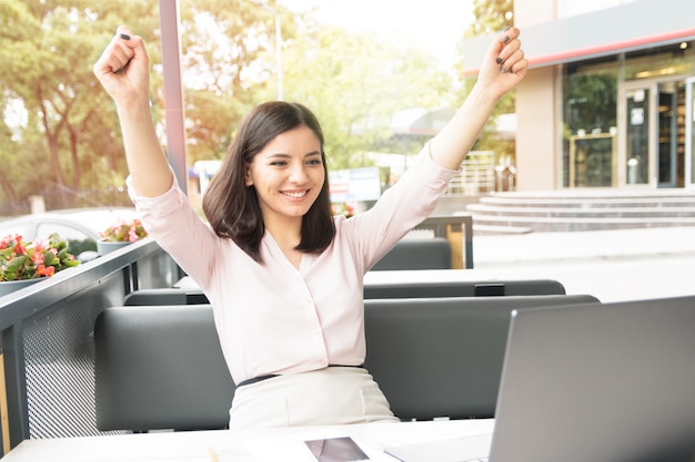 Jonge vrouw met laptop in café dat zeer tevreden en succesvol is.