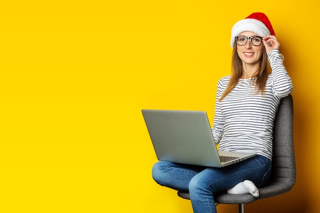 Jonge vrouw met laptop, in een kerstmuts en zit op een stoel