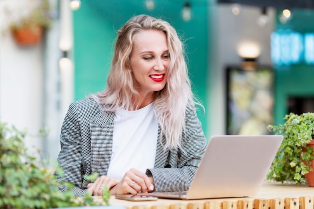 Jonge vrouw met laptop in een straat zomercafé. Mooie glimlachende blonde met lang haar.