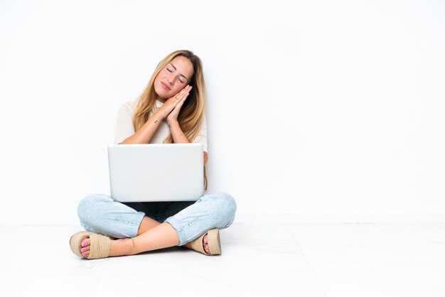 Jonge vrouw met laptop zittend op de vloer geïsoleerd op een witte achtergrond slaap gebaar maken in dorable expressie