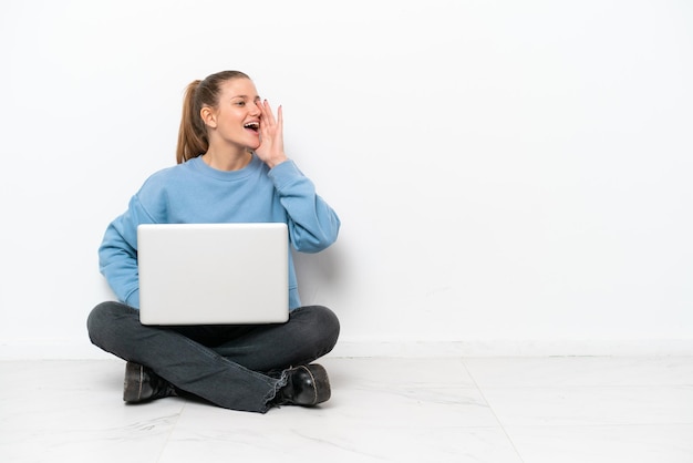 Jonge vrouw met laptop zittend op de vloer schreeuwen met mond wijd open voor de laterale