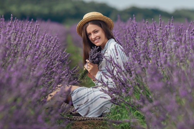 Jonge vrouw met lavendelboeket op de violette achtergrond van het bloemengebied