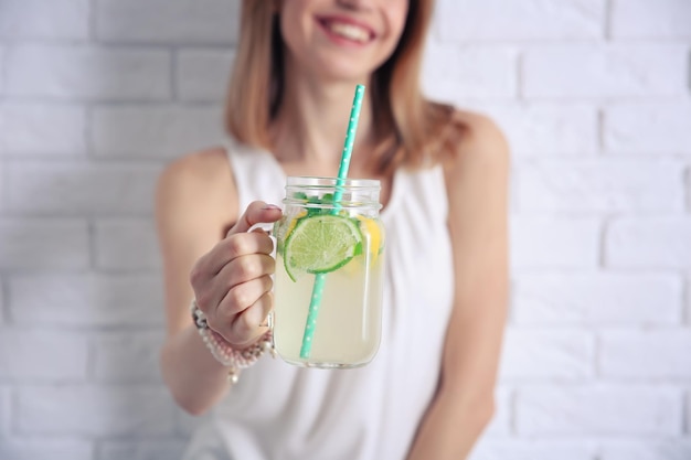 Jonge vrouw met limonade dichtbij lichte bakstenen muurclose-up