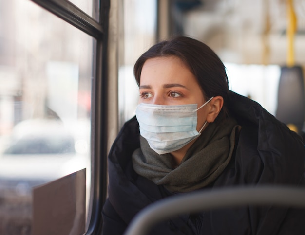 Jonge vrouw met medisch masker in stadsvervoer, bus, herfstkleding