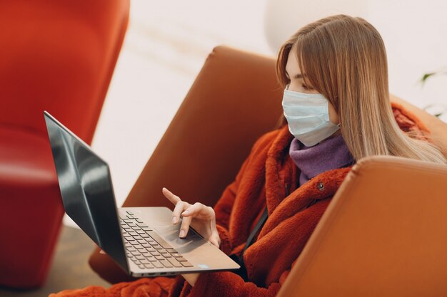 Jonge vrouw met medische masker en laptop in een stoel