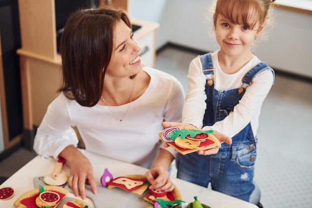 Jonge vrouw met meisje samen spelen met speelgoed op de keuken