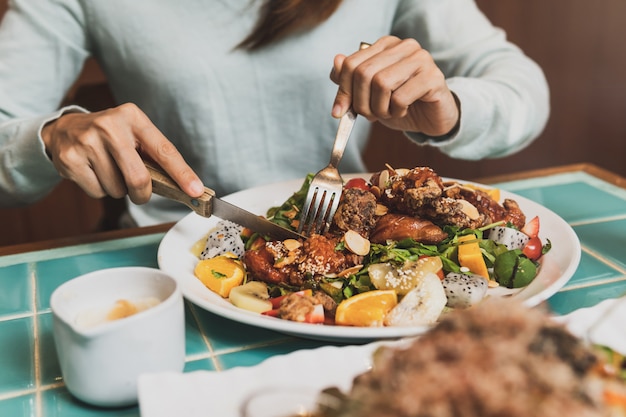 Jonge vrouw met mes en vork aan het snijden van vlees in restaurant