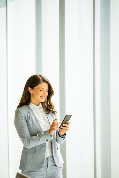 Jonge vrouw met mobiele telefoon bij het raam