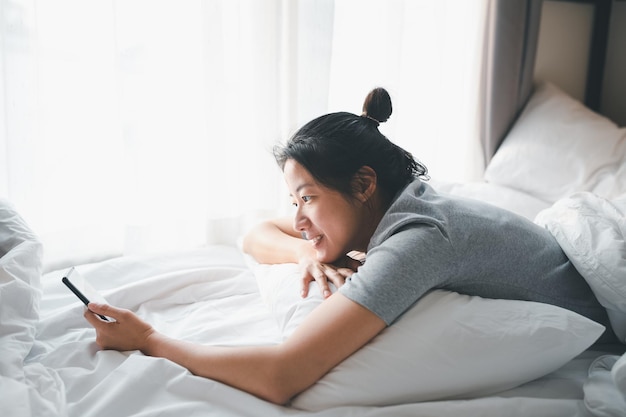 Jonge vrouw met mobiele telefoon terwijl ze op bed ligt